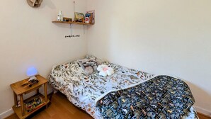 A bedroom with a bed, a small bedside table with a lamp, a wall-mounted shelf with books, and a decorative deer head.