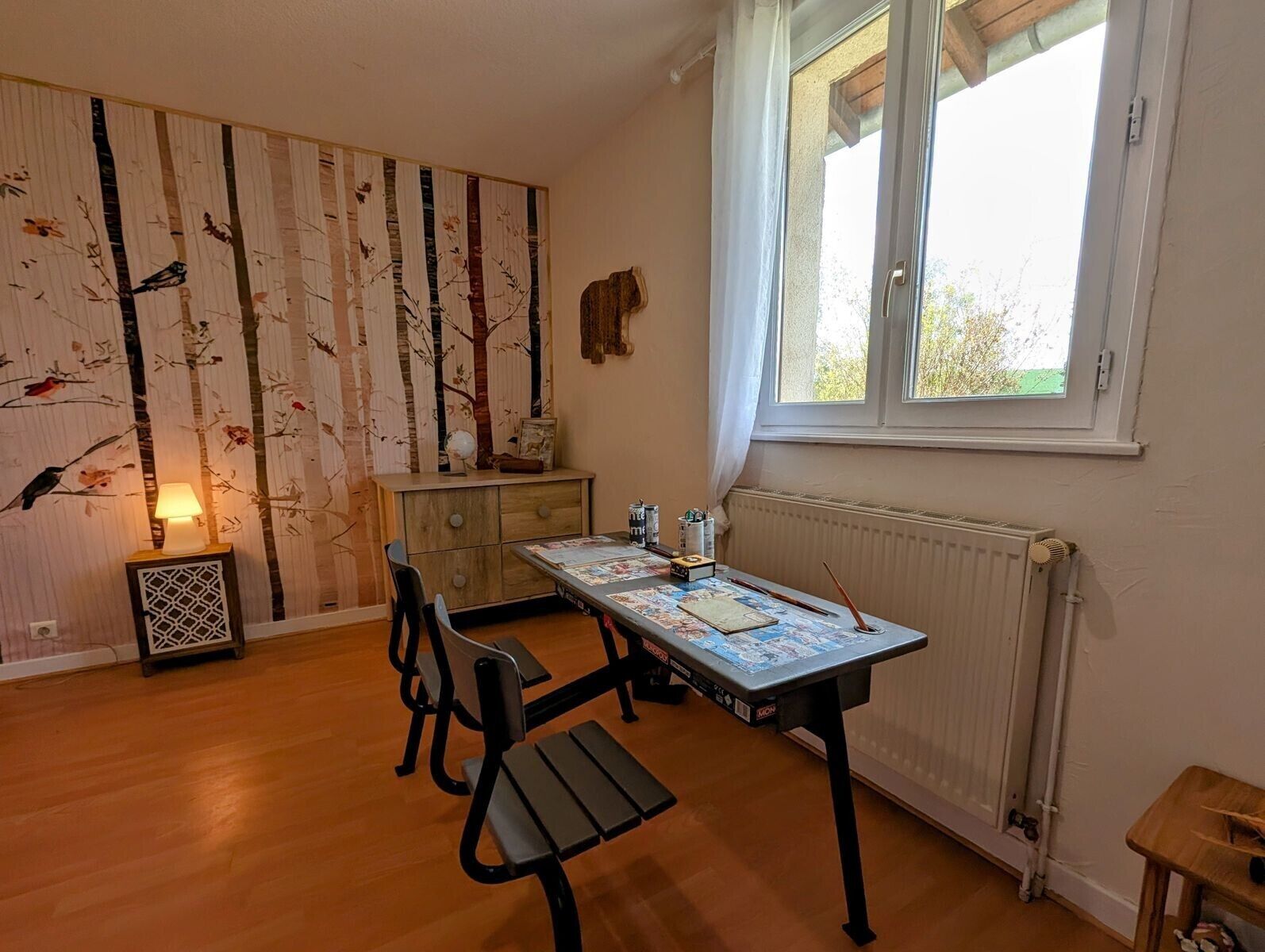 Huoneessa on puulattia, pöytä, jossa on kartta, tuoli, patteri ja ikkuna, jossa on verhot.