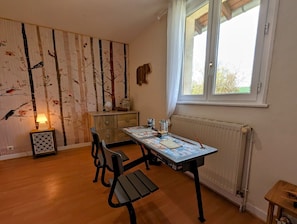 Ett rum med trägolv, ett bord med en karta, en stol, ett element och ett fönster med gardiner.