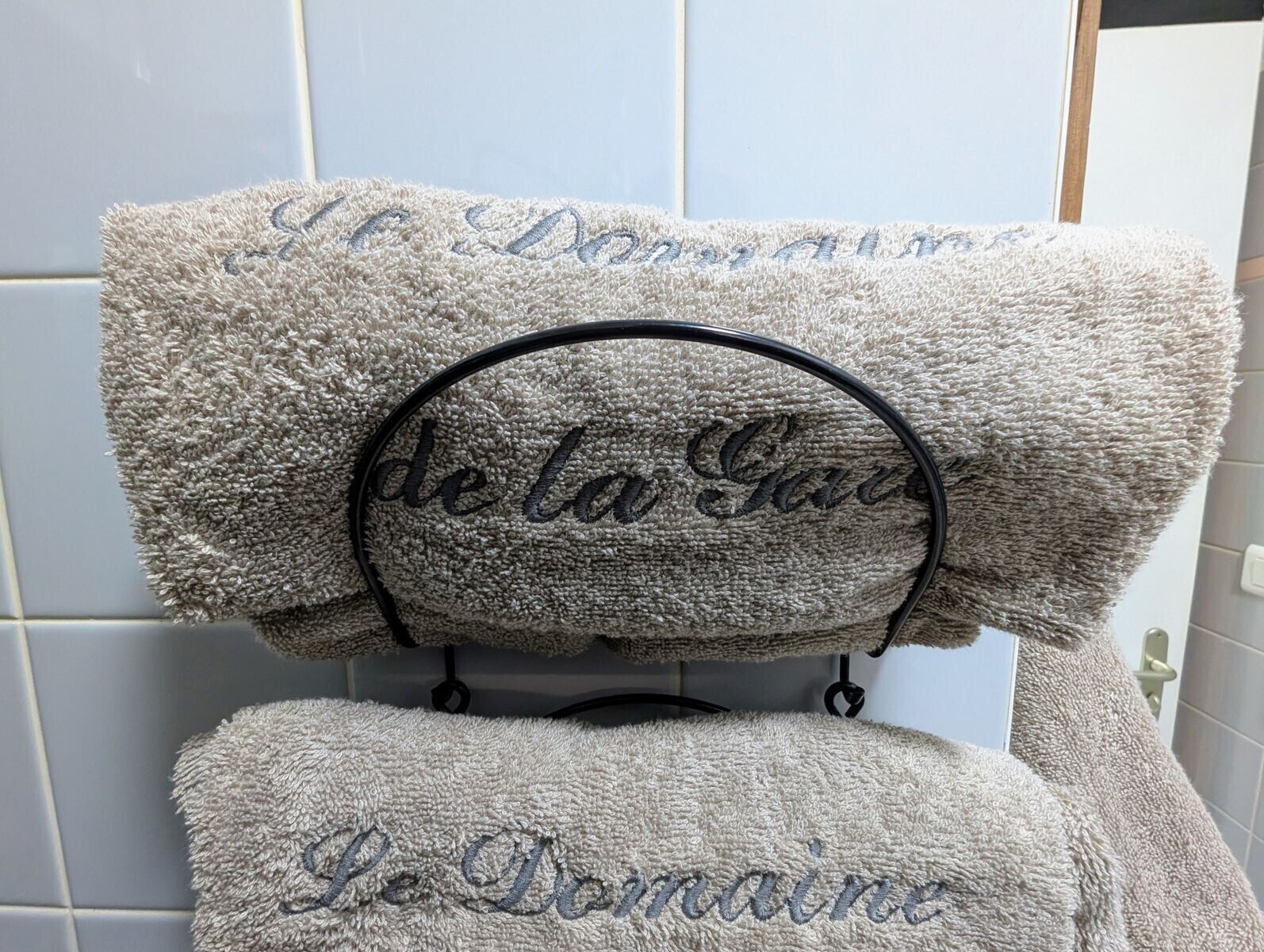 A bathroom with a towel rack holding two towels, one with 'Le Domaine' embroidered on it.