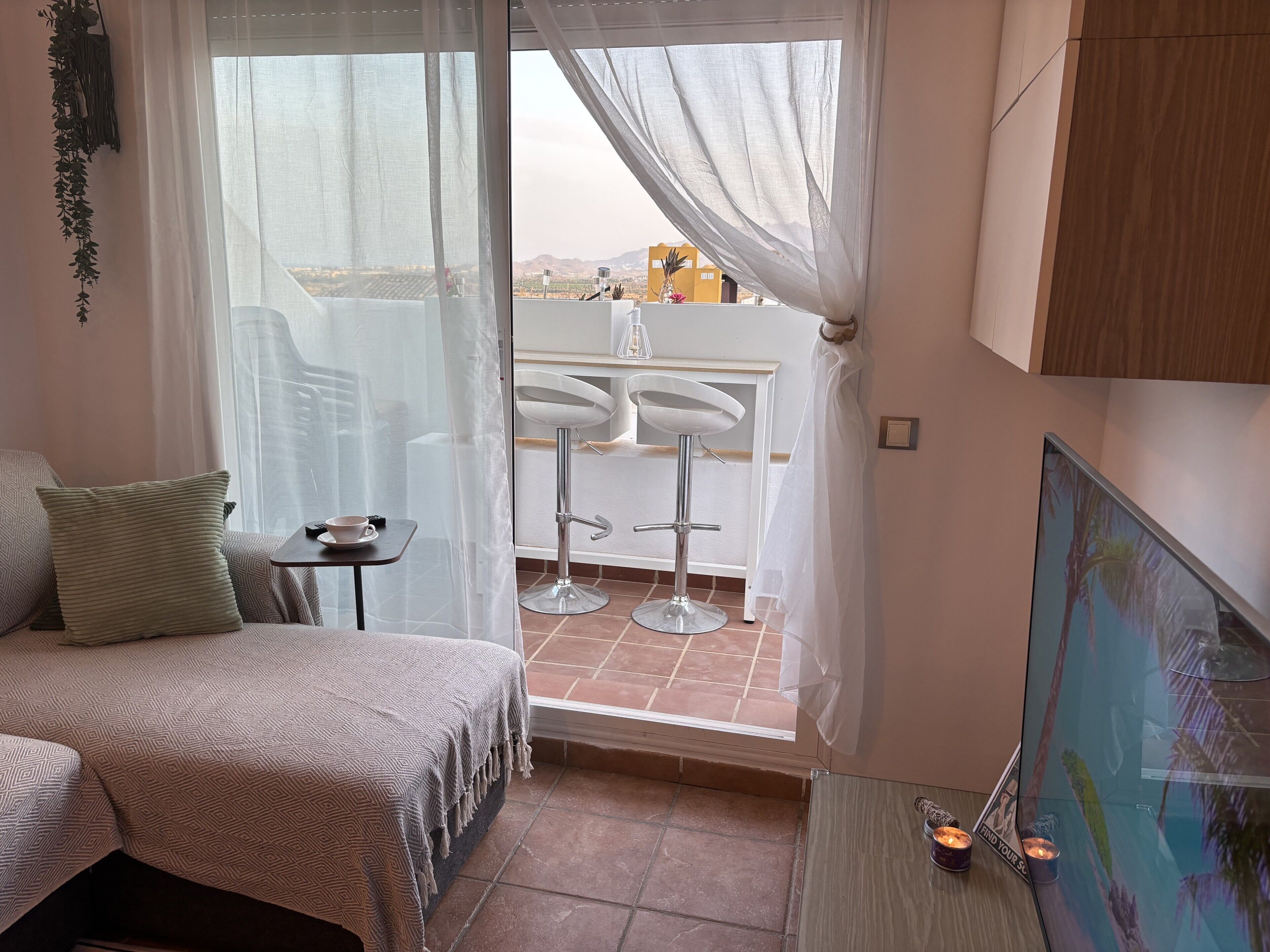 Un dormitorio con una cama, una mesita con una taza y un balcón con sillas y una mesa blancos.