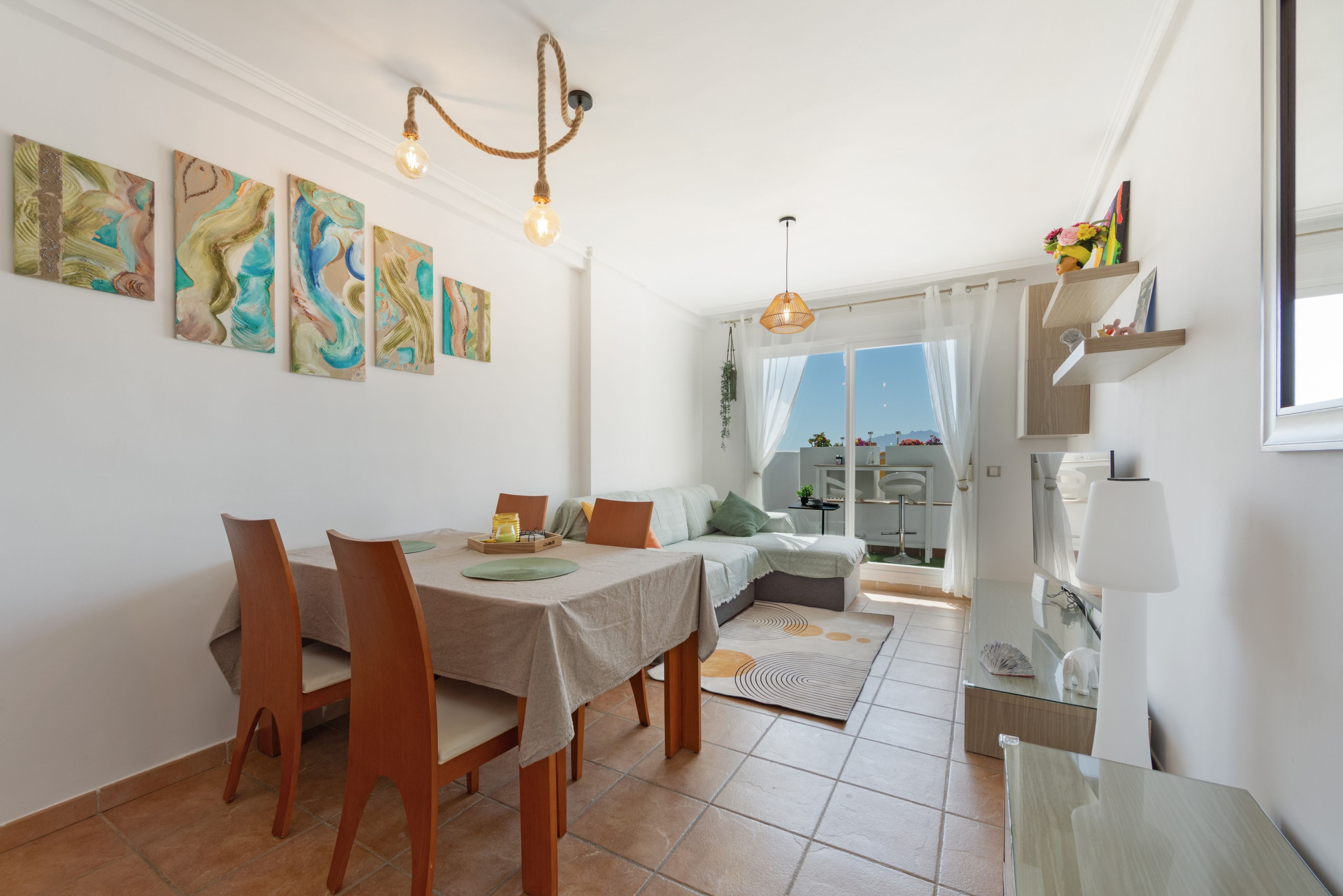 A dining area with a table and chairs, a sofa, and a view through a window.