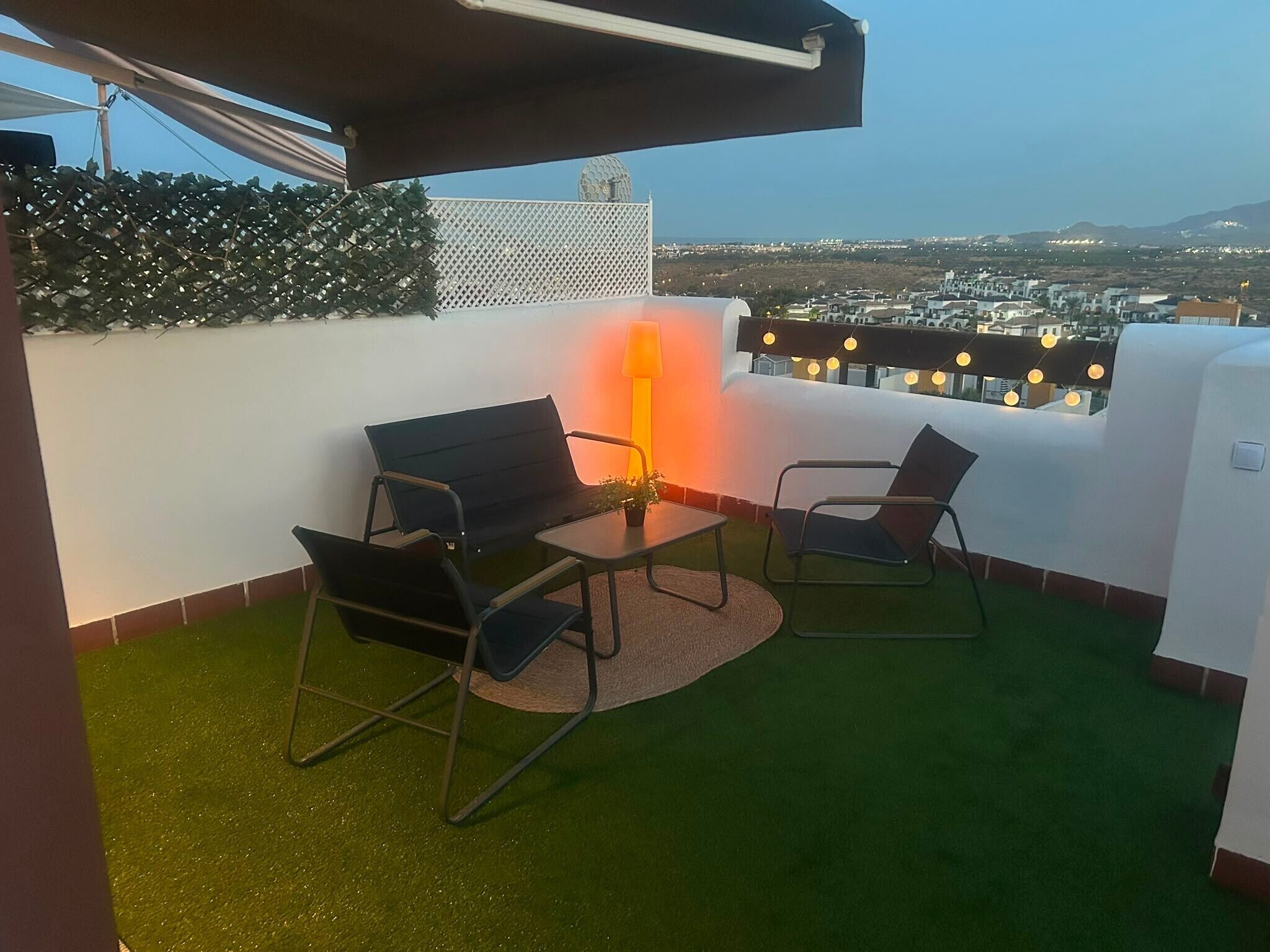 Una terraza en la azotea con dos sillas, una mesa y una planta en maceta.