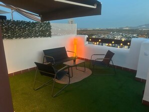 A rooftop terrace with two chairs, a table, and a potted plant.