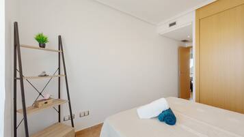 A bedroom with a bed, a wooden wardrobe, a metal shelf unit with a plant, and a small wooden box.