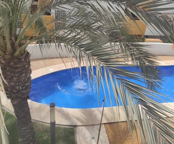 A swimming pool surrounded by palm trees and a building with a yellow facade.