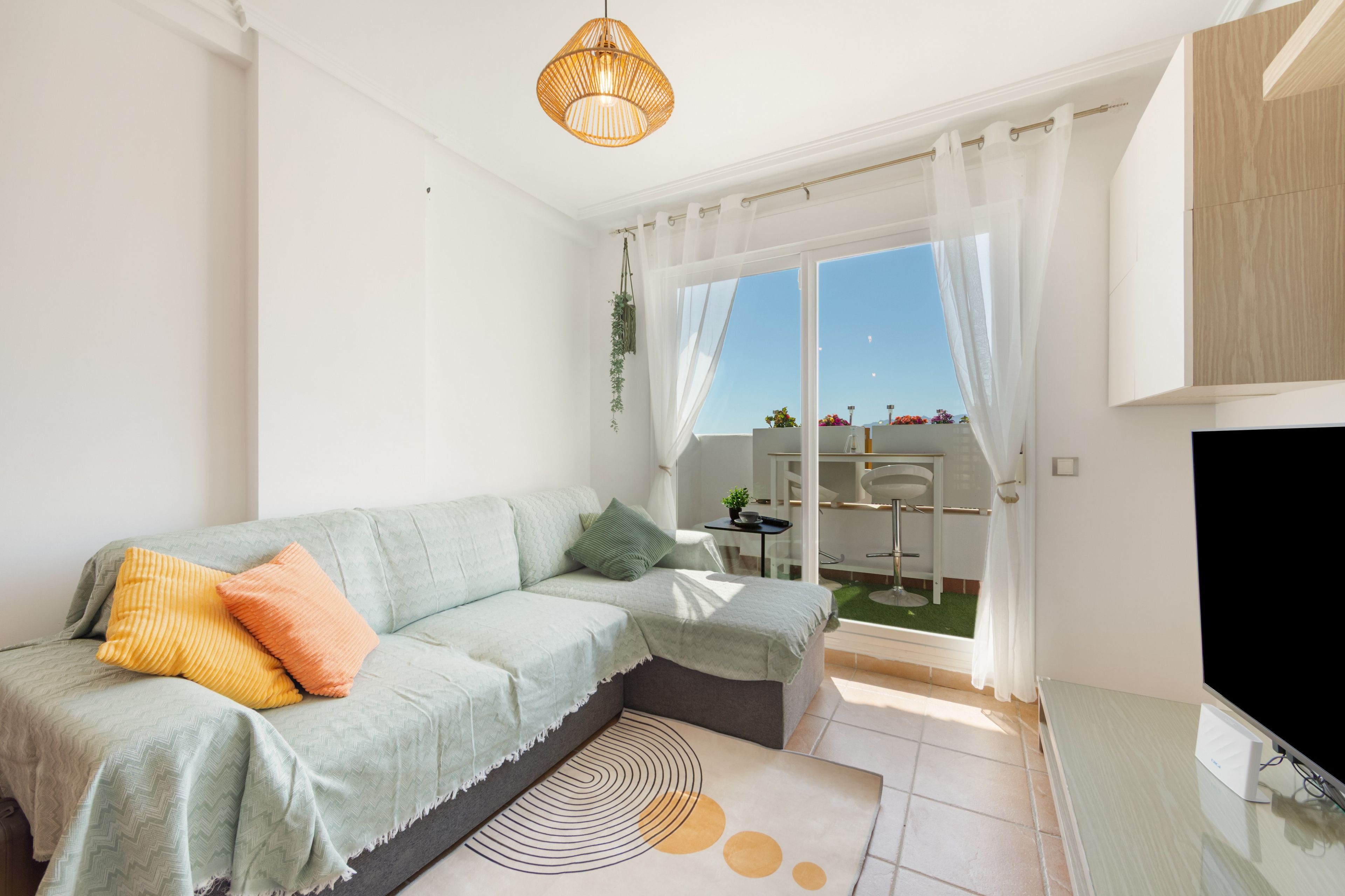 A modern living room with a sofa, a television, and a view of the outdoors.