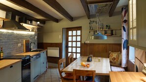 A kitchen with a wooden table, chairs, and a dining area with a view of the outdoors. - Cottage "Le Moulin de Laval" with Private Terrace, Wi-Fi, and Air Conditioning (Saint-Priest-des-Champs)