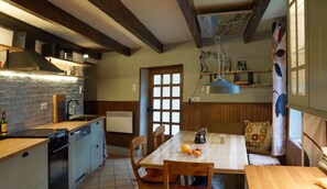 A kitchen with a wooden table, chairs, and a dining area with a view of the outdoors. - Cottage "Le Moulin de Laval" with Private Terrace, Wi-Fi, and Air Conditioning (Saint-Priest-des-Champs)