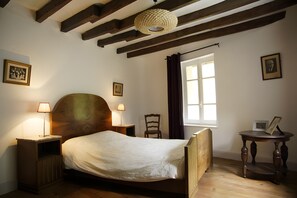 A bedroom with a wooden bed, two bedside lamps, a window with curtains, and a framed picture on the wall. - Cottage "Le Moulin de Laval" with Private Terrace, Wi-Fi, and Air Conditioning (Saint-Priest-des-Champs)