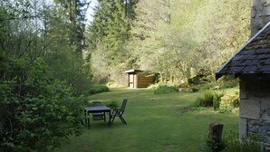 A rustic wooden shed in a lush garden with a table and chairs. - Cottage "Le Moulin de Laval" with Private Terrace, Wi-Fi, and Air Conditioning (Saint-Priest-des-Champs)