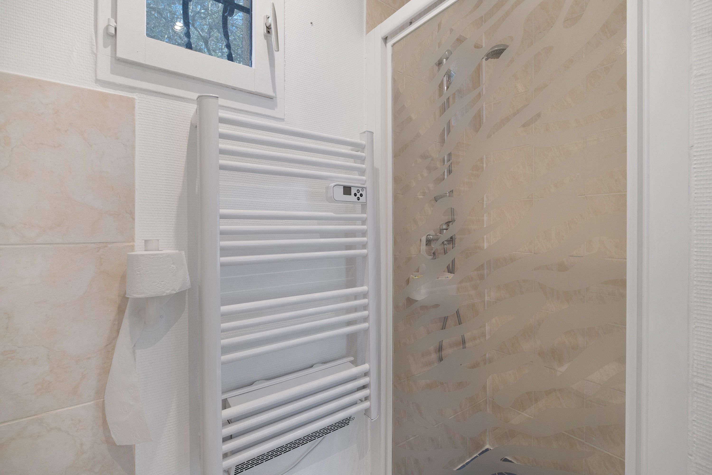 Une salle de bain avec un porte-serviettes blanc, un support pour le papier toilette et un espace douche avec un mur carrelé.