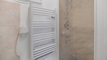 Une salle de bain avec un porte-serviettes blanc, un support pour le papier toilette et un espace douche avec un mur carrelé.