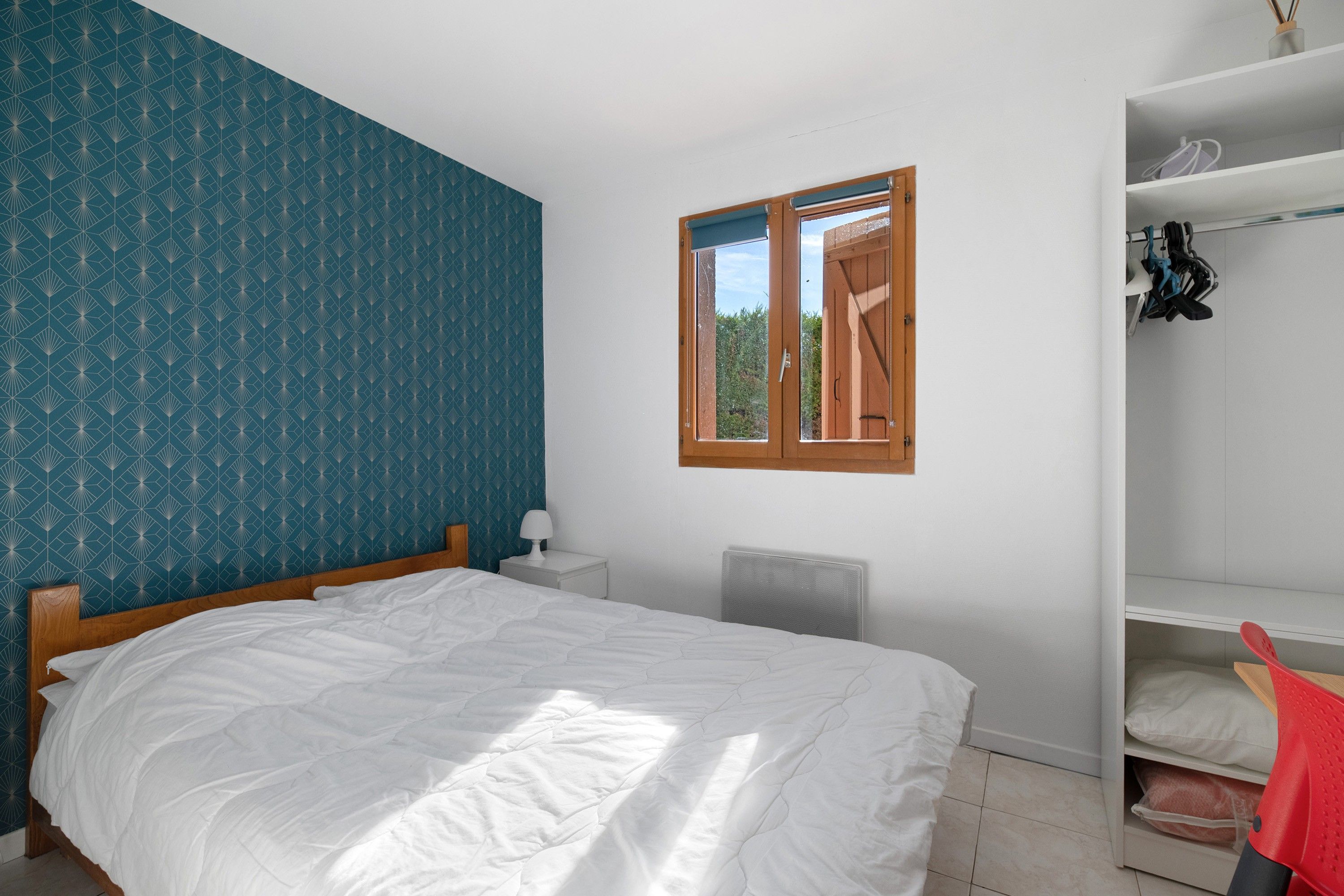 Une chambre à coucher comprenant un lit, une table de chevet, un radiateur, une armoire et une fenêtre donnant sur un paysage verdoyant.