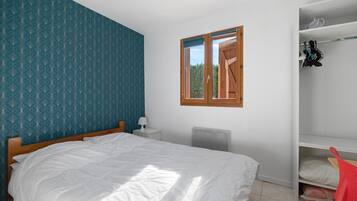 Une chambre à coucher comprenant un lit, une table de chevet, un radiateur, une armoire et une fenêtre donnant sur un paysage verdoyant.