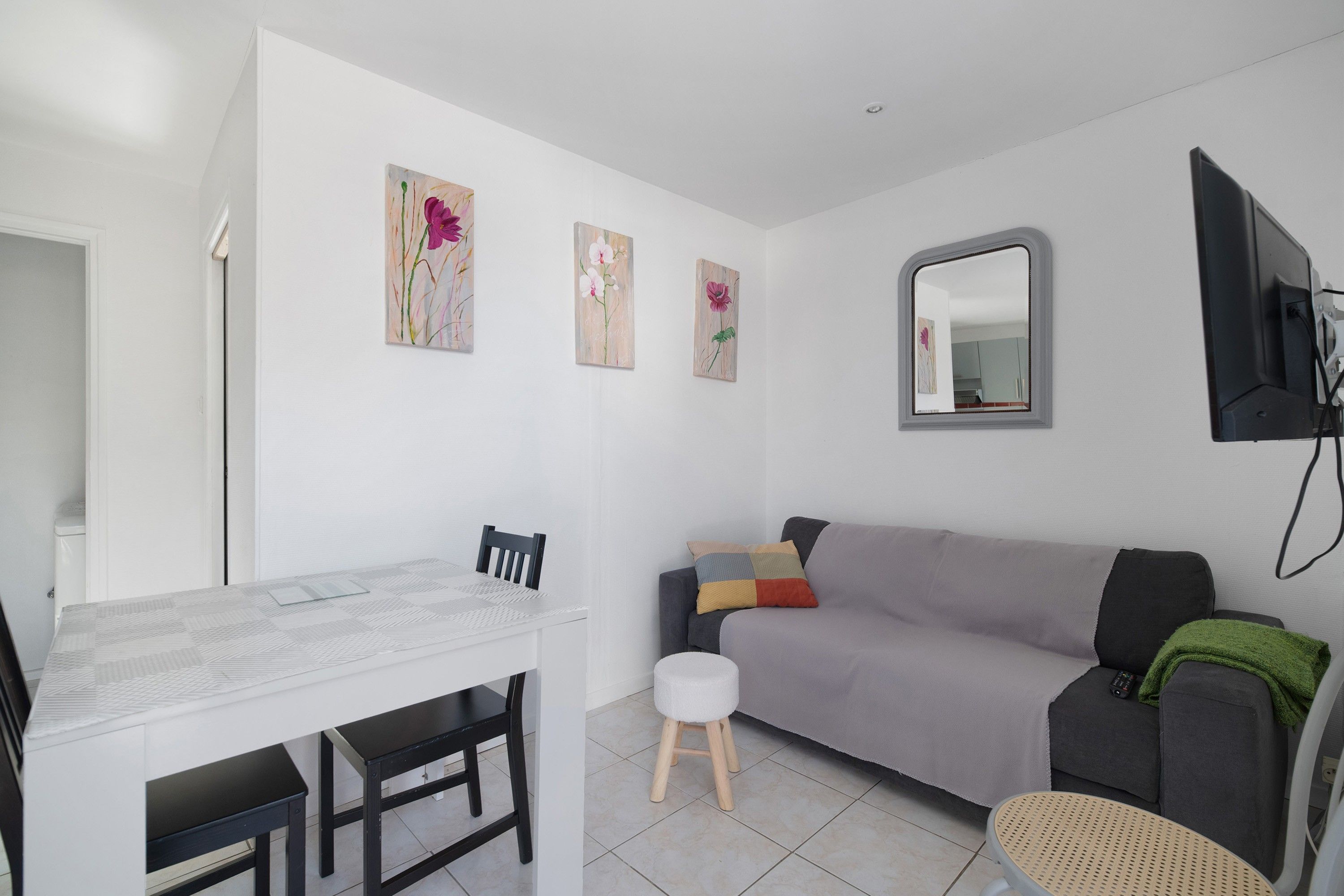 Una sala de estar moderna con una pared blanca, un sofá gris, una pequeña mesa redonda y una mesa de centro blanca.