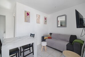 A modern living room with a white wall, a grey sofa, a small round table, and a white coffee table.