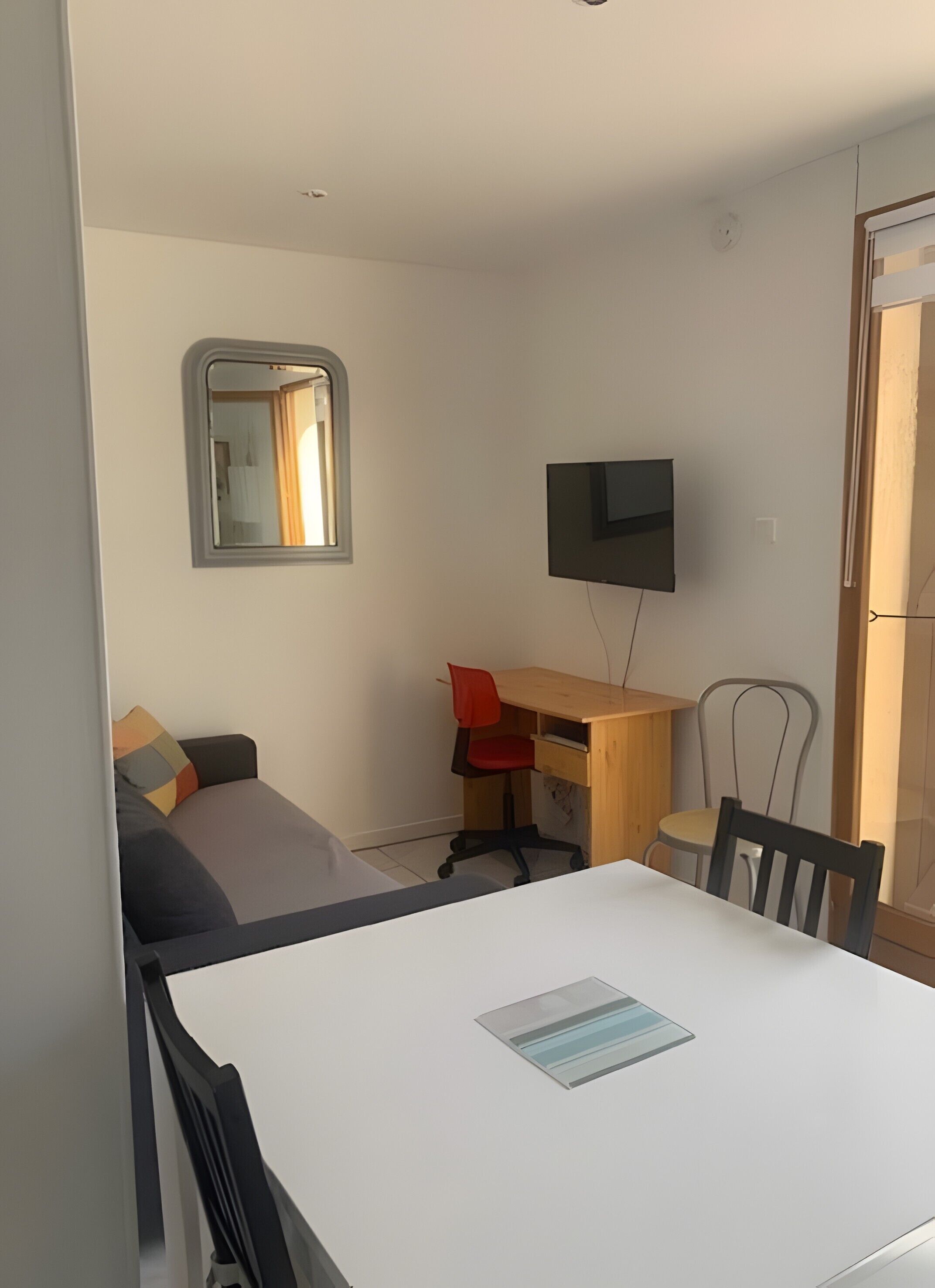 Una habitación pequeña con cama, escritorio, silla, televisor y ventana.