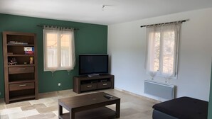 Ein Wohnzimmer mit Fernseher, einer Couch, einem Couchtisch und einem Bücherregal.