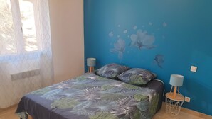 Ein Schlafzimmer mit einem Bett, zwei Nachttischlampen, einer Wandmalerei und einem Fenster mit Vorhang.