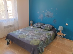 Ein Schlafzimmer mit einem Bett, zwei Nachttischlampen, einer Wandmalerei und einem Fenster mit Vorhang.