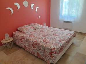 A bedroom with a bed, a round table with a lamp, and a wall with crescent moon decorations. - Villa Les Cigales: Mountain View, Wi-Fi, Air Conditioning (Chamborigaud)