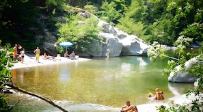 Ein natürlicher Pool, umgeben von Steinen und Bäumen, mit badenden und sonnenden Personen.