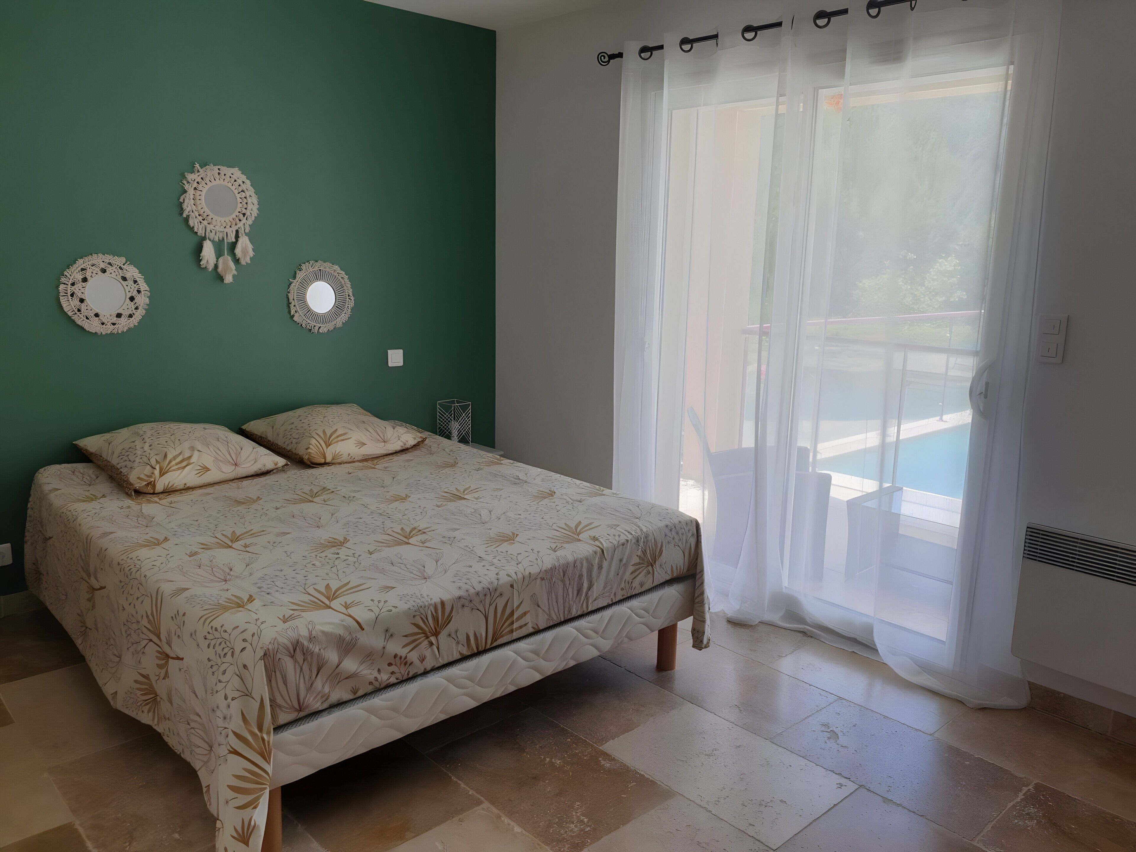 Une chambre à coucher avec un lit, des murs verts, des miroirs décoratifs et une vue sur une piscine par la fenêtre.
