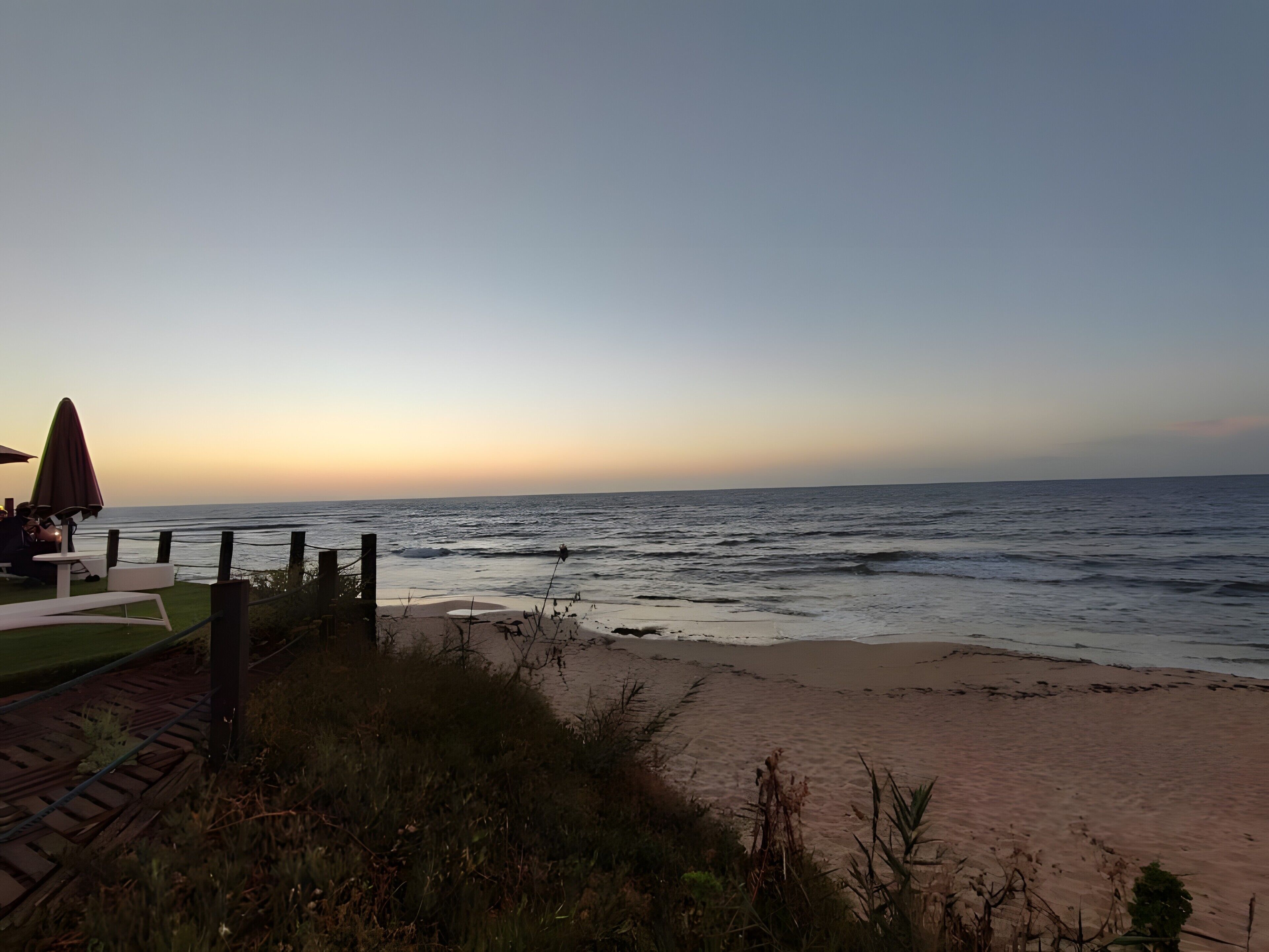 A beach with a wooden fence, a table with chairs, and a view of the ocean.