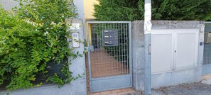 A gated entrance with a metal gate, a brick pathway, and a wall with a utility box and a sign.
