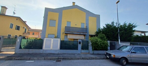 A two-story building with a flat roof, a gated entrance, and a parked car in front.