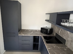 Une cuisine avec des meubles de couleur sombre, un plan de travail en marbre et un four encastré.