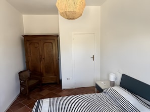 A bedroom with a bed, a wardrobe, a chair, a bedside table with a lamp, and a hanging light fixture. - Holiday Home 'Il Casalino - Bilo 1' with Sea View and Air Conditioning (Marina di Campo)