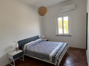 Une chambre à coucher comprenant un lit, des tables de chevet, une lampe suspendue, une fenêtre et un appareil de climatisation.