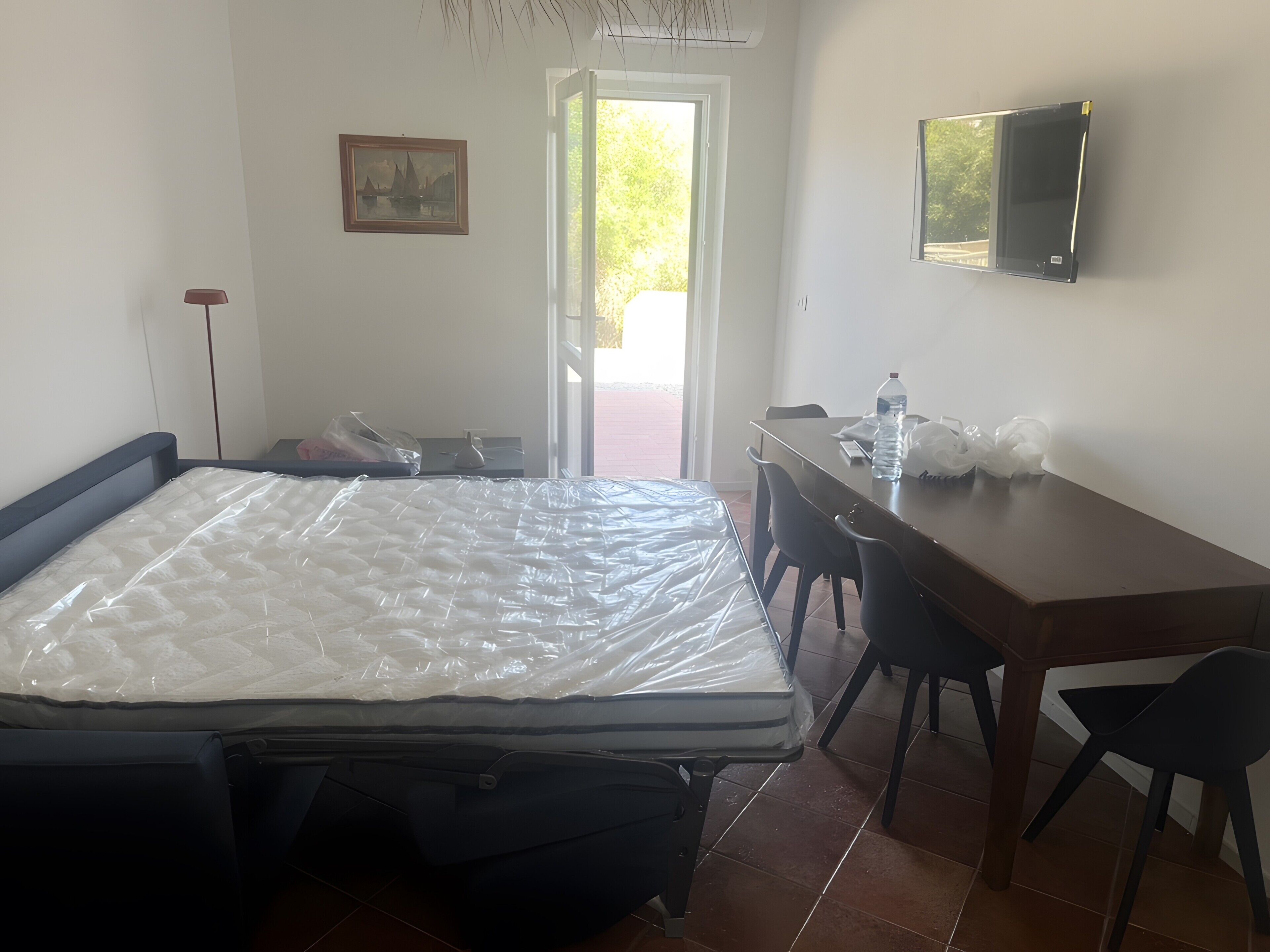 Una habitación con cama, escritorio, silla, televisor y puerta que da al exterior.