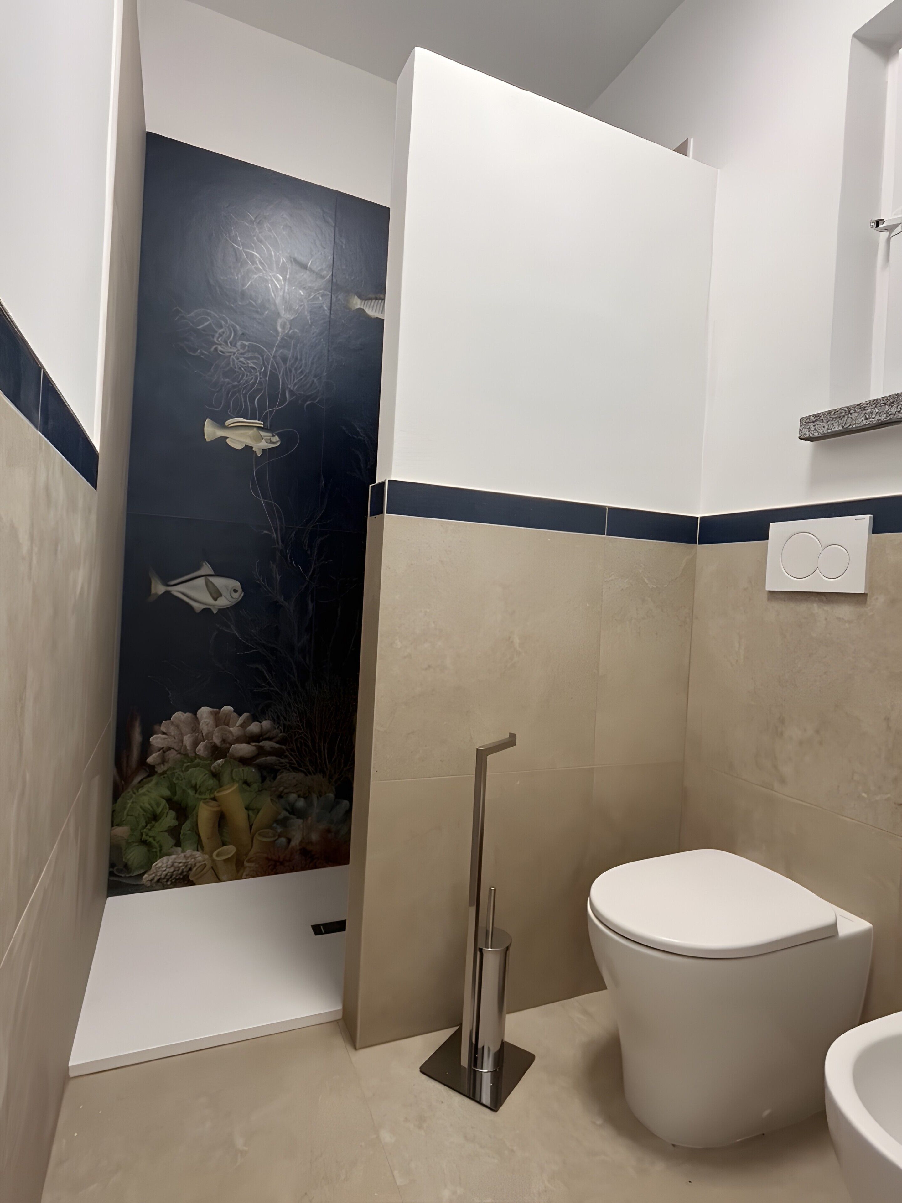 Une salle de bain équipée de toilettes, d’une douche et ornée d’une fresque murale représentant des poissons et des plantes aquatiques.