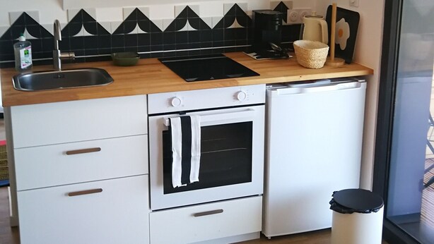 A compact kitchen with a sink, stove, oven, and a trash bin.