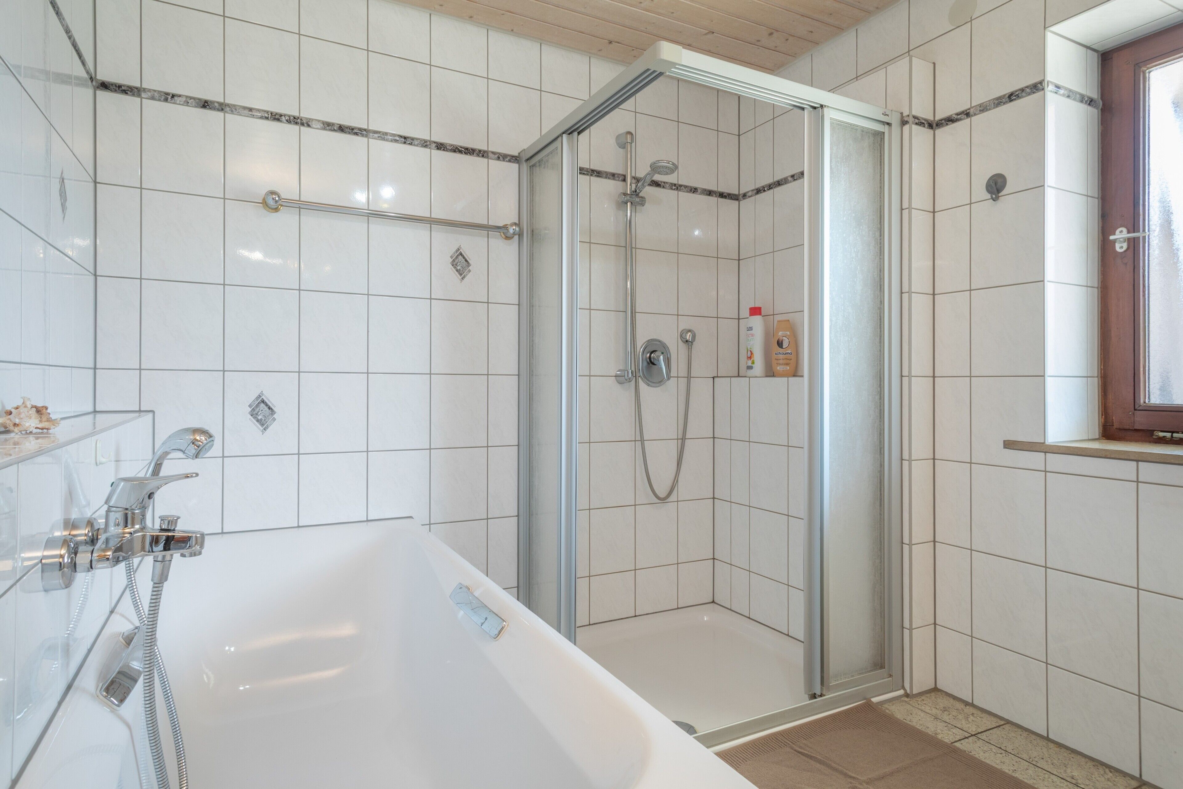 Ein modernes Badezimmer mit einer gläsernen Duschkabine, einer freistehenden Badewanne und einem kleinen Ablagefach für Toilettenartikel.