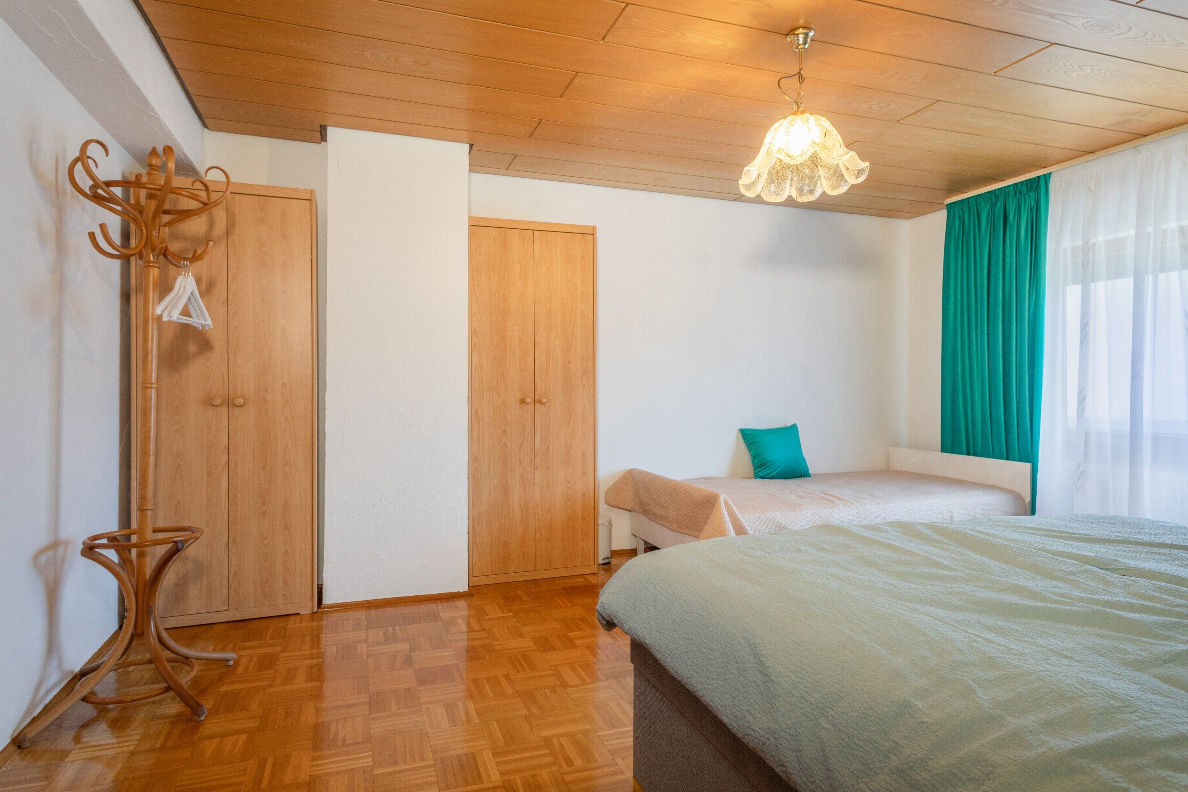 A bedroom with a wooden floor, a bed, a wardrobe, and a hanging coat rack.