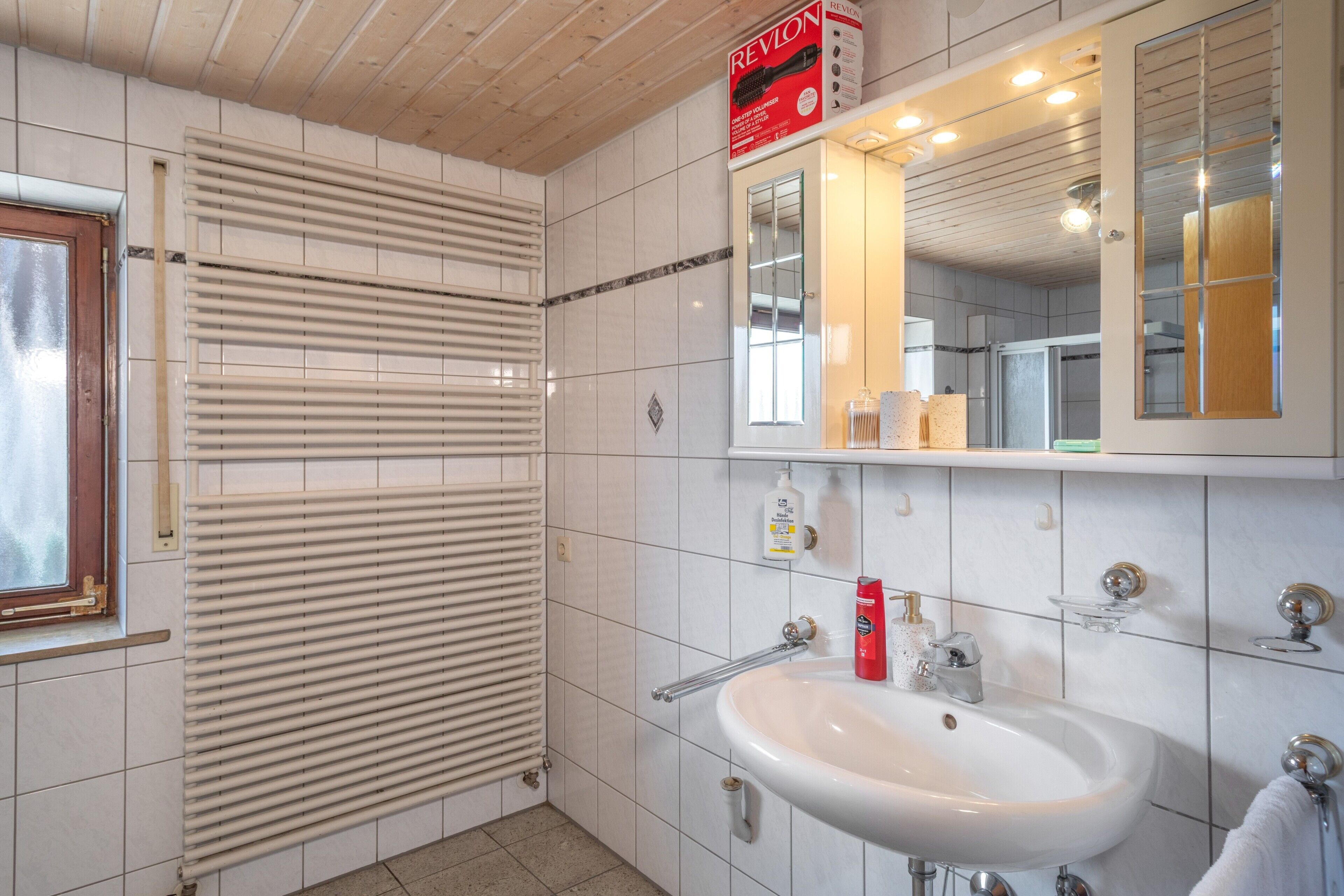 Une salle de bain avec un lavabo blanc, un miroir et une fenêtre.