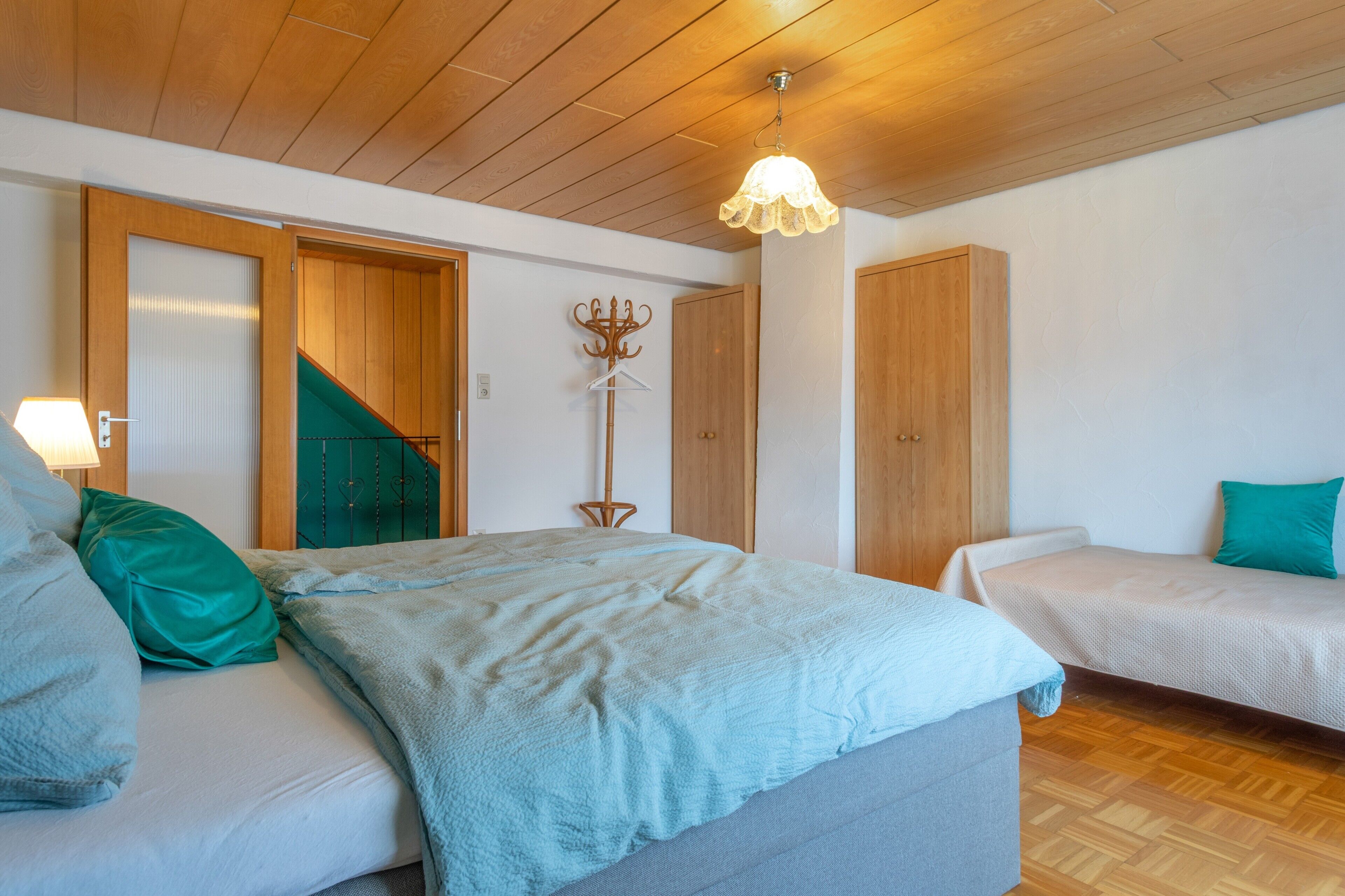 Un dormitorio con una cama, dos mesitas de noche, un perchero y un armario de madera.