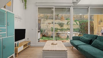 Una sala de estar con televisión, una mesa de centro de madera, un sofá verde y un ventanal corredero que da a un jardín.