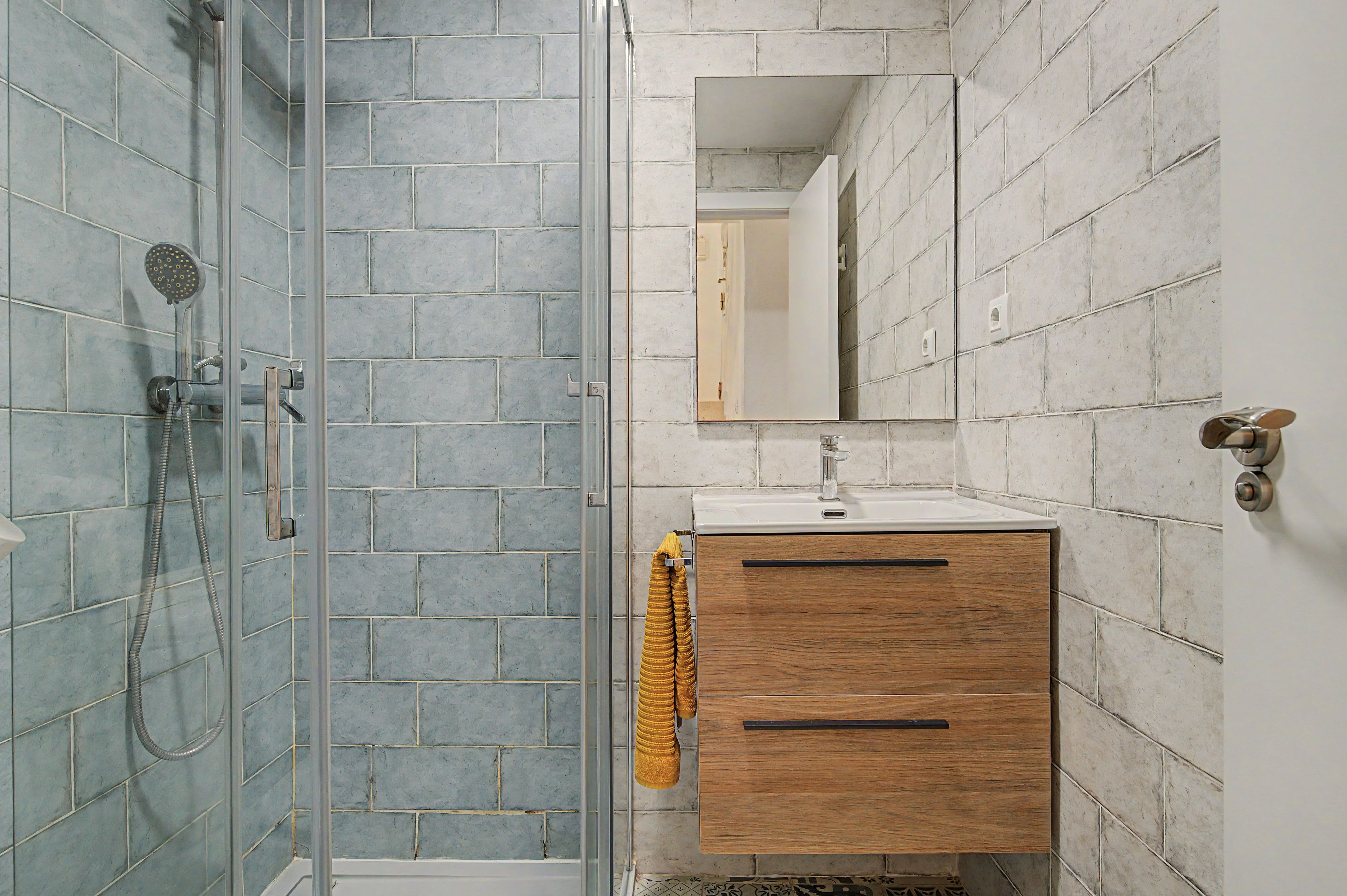 Un baño con cabina de ducha de vidrio, tocador de madera con espejo y una toalla colgada en la pared.