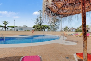 Una piscina amb vora de rajola, envoltada de gandules i un parasol de palla.
