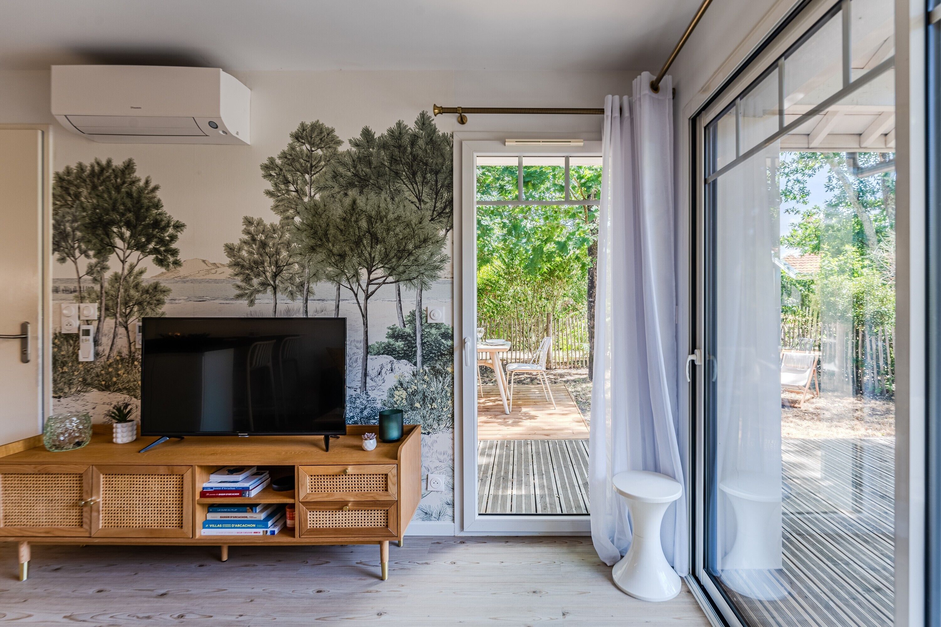 A modern living room with a flat-screen TV, wooden furniture, and a view of the outdoors.