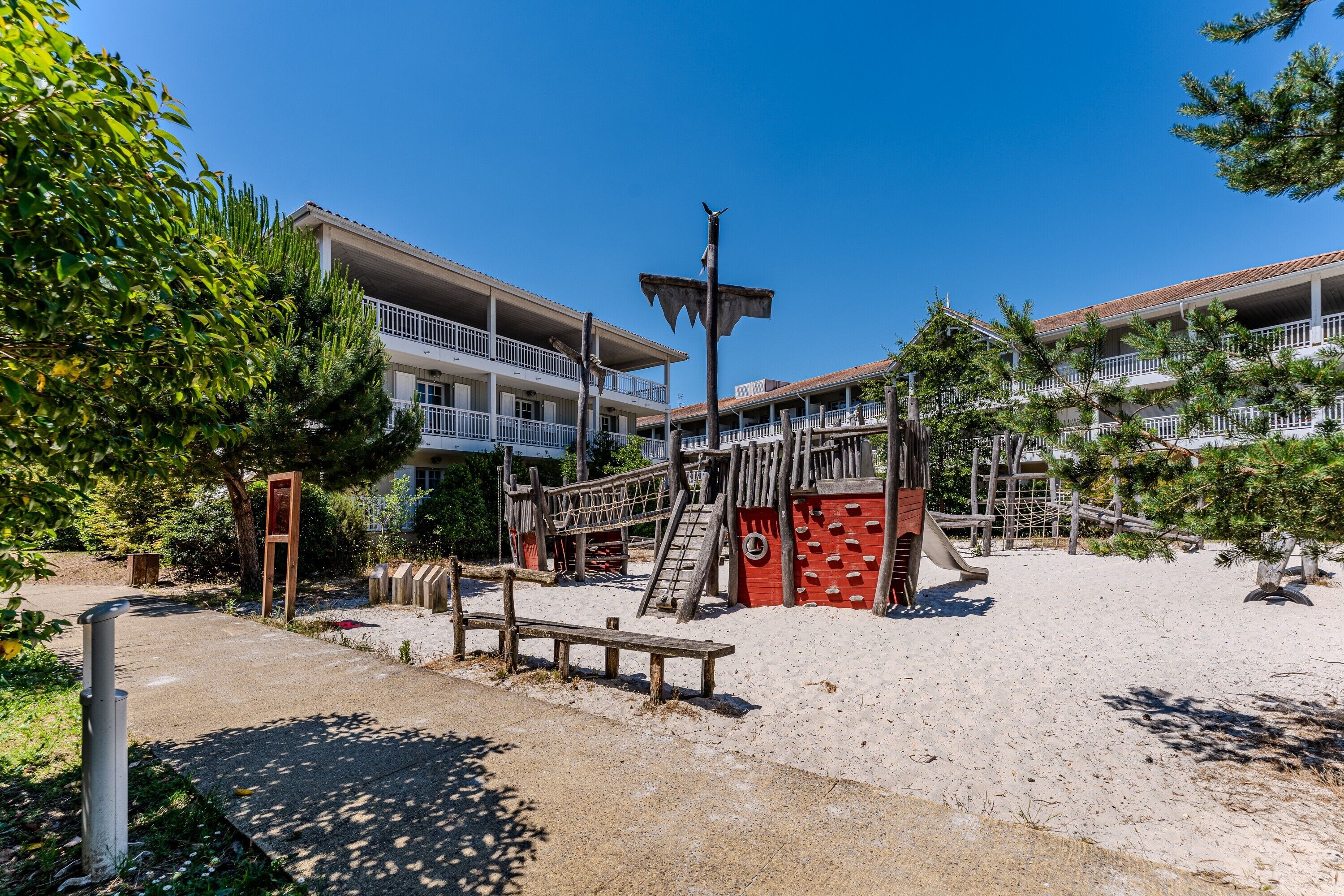 Un hôtel situé en bord de mer, doté d’une aire de jeux, d’un banc en bois et surplombant un ciel bleu dégagé.