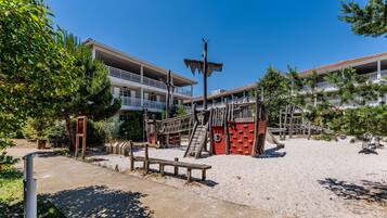 Un hôtel situé en bord de mer, doté d’une aire de jeux, d’un banc en bois et surplombant un ciel bleu dégagé.