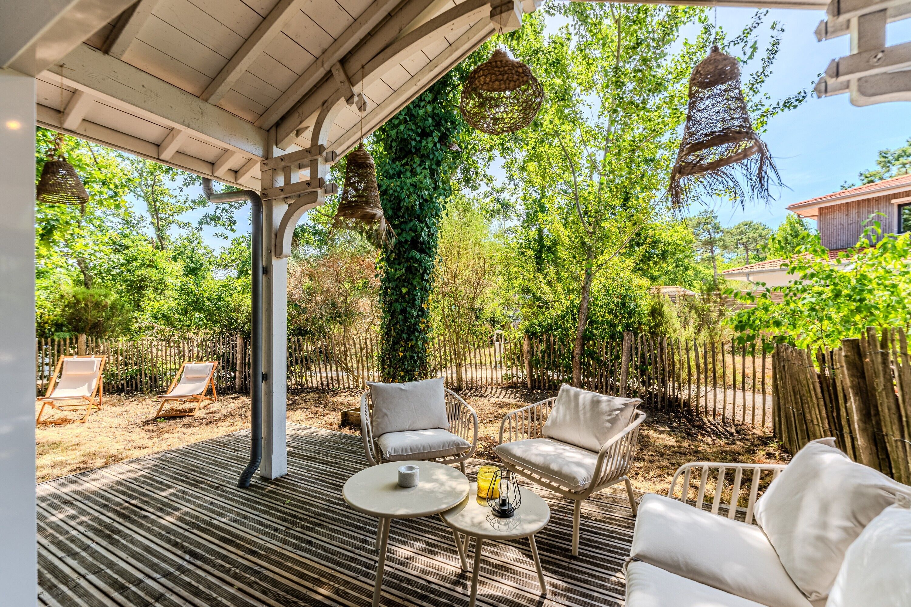 Un espace extérieur aménagé, abrité et doté d’une pergola, d’une terrasse en bois et d’une vue sur une propriété résidentielle.