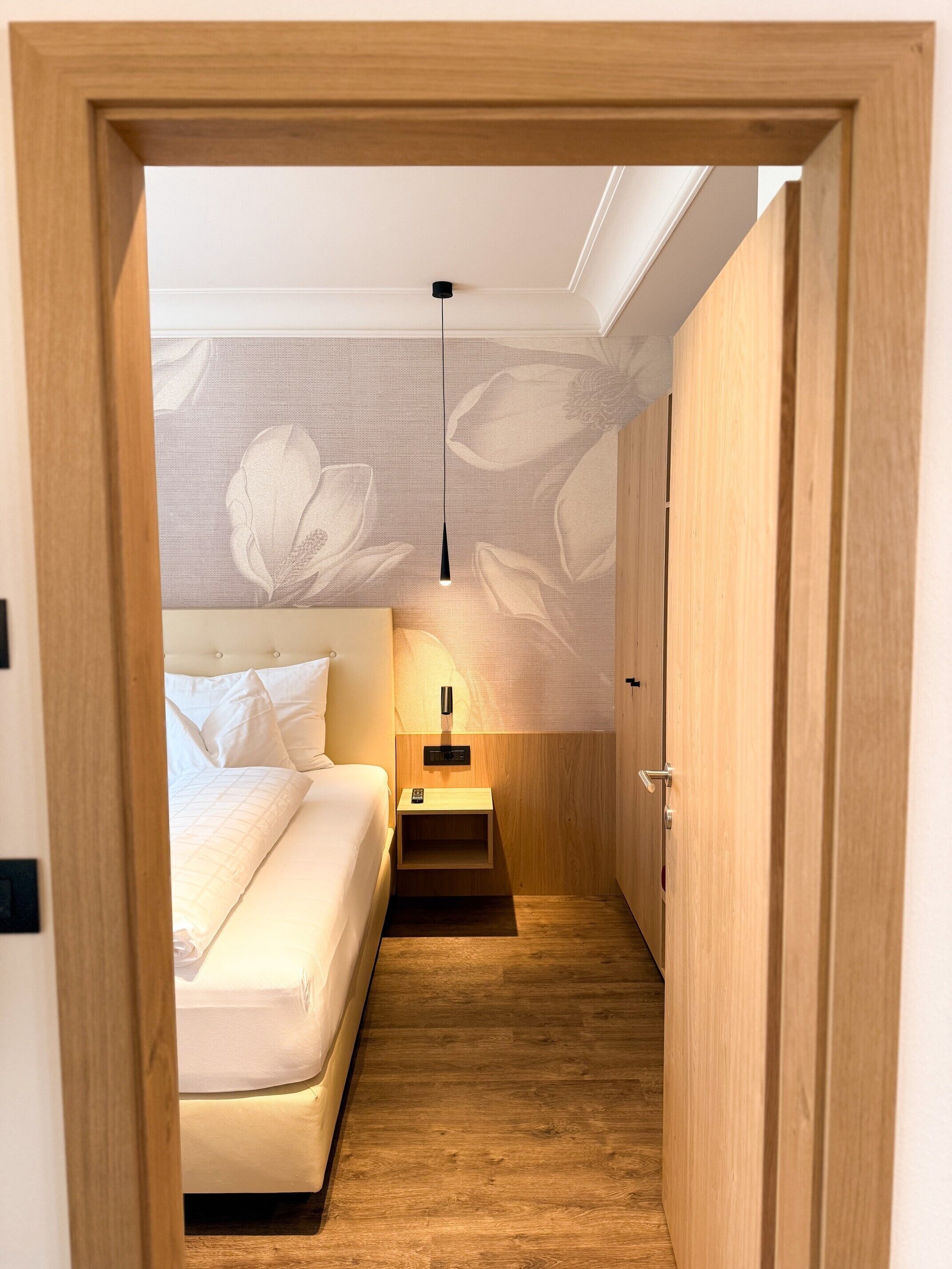 Un pasillo estrecho que conduce a un dormitorio con cama, mesita de noche y una lámpara colgante.