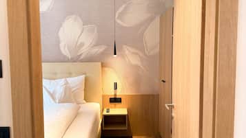 Un pasillo estrecho que conduce a un dormitorio con cama, mesita de noche y una lámpara colgante.